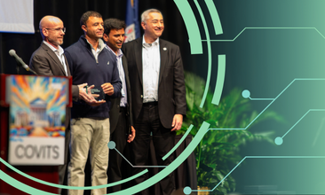 A team of four men stand on stage. Three of the men are accepting a glass award. There is a podium with a 'COVITS 2025' sign in the foreground.